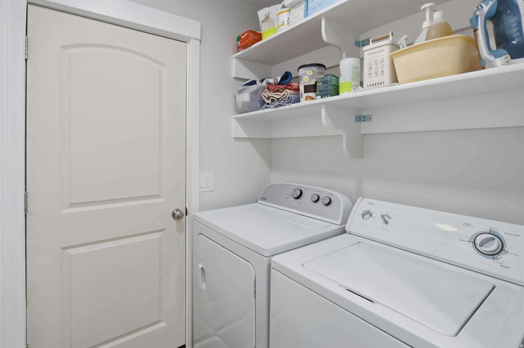 Dedicated laundry space featuring a white door with arched paneling, white walls, and built-in shelving