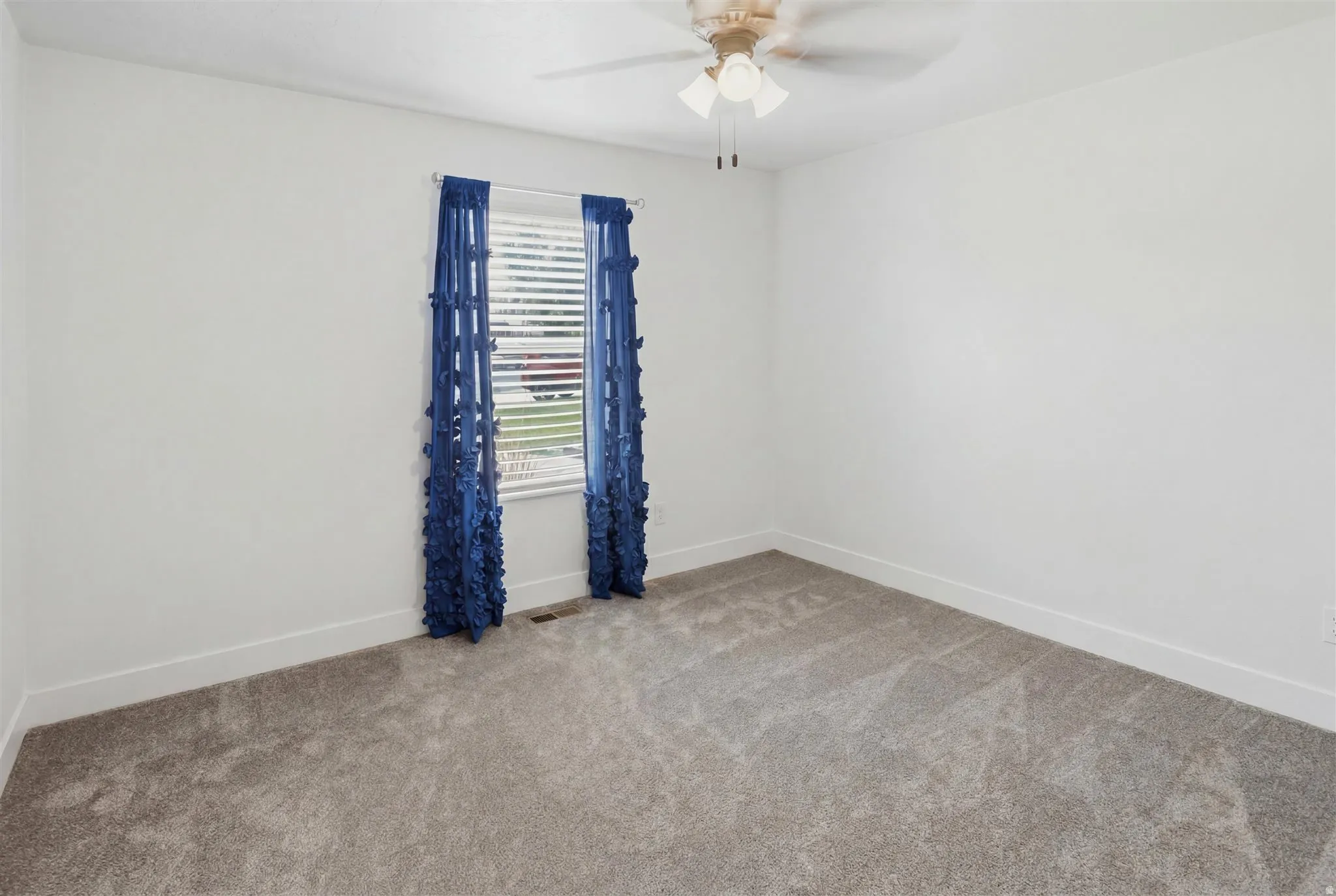 Carpeted room featuring a window with horizontal blinds, a ceiling fan with integrated lighting, and white baseboards