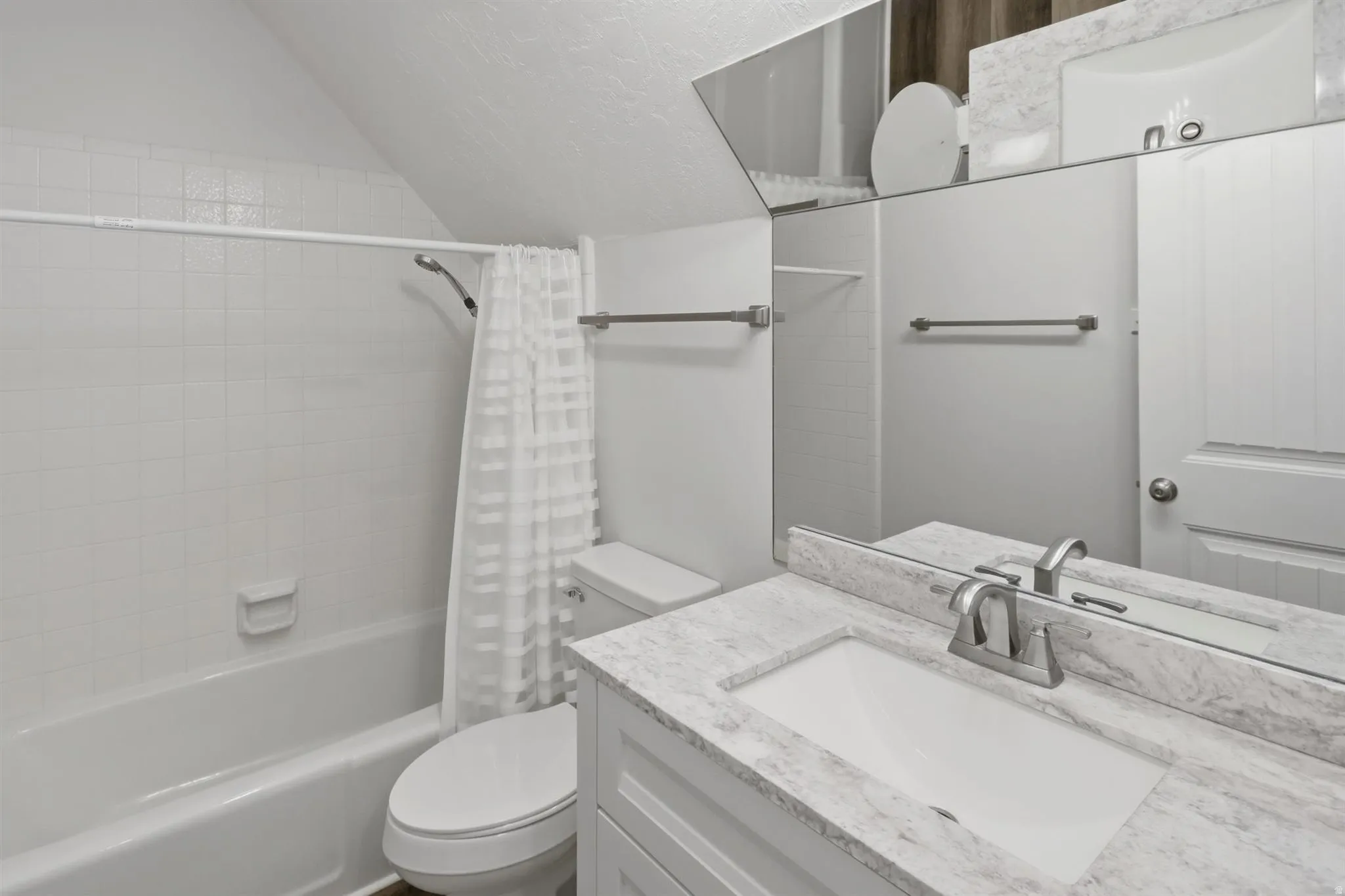 Bathroom featuring a single vanity with a white countertop and undermount sink, a toilet, a shower-over-tub combination with white subway tile surround, and a wall-mounted mirror