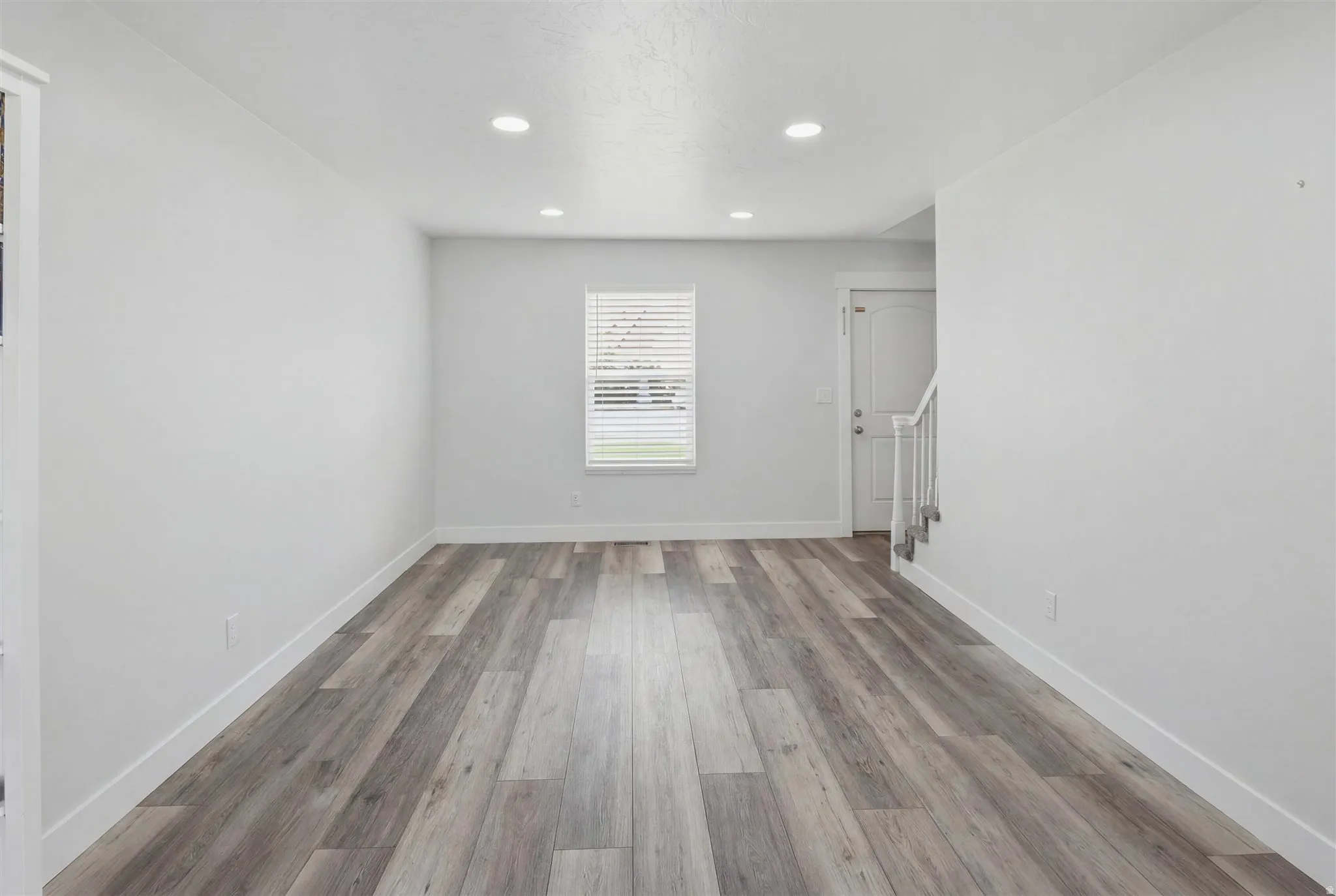 Spacious room with wood-finish flooring, white baseboards, and neutral wall tones