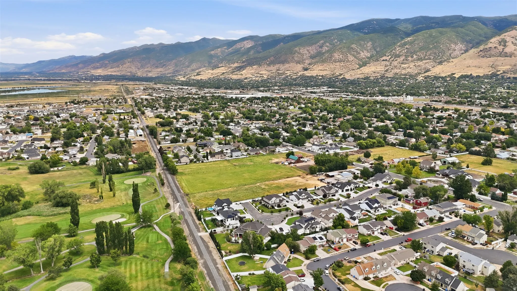 Expansive aerial view of a residential area featuring a golf course, mountain backdrop, and tree-lined streets