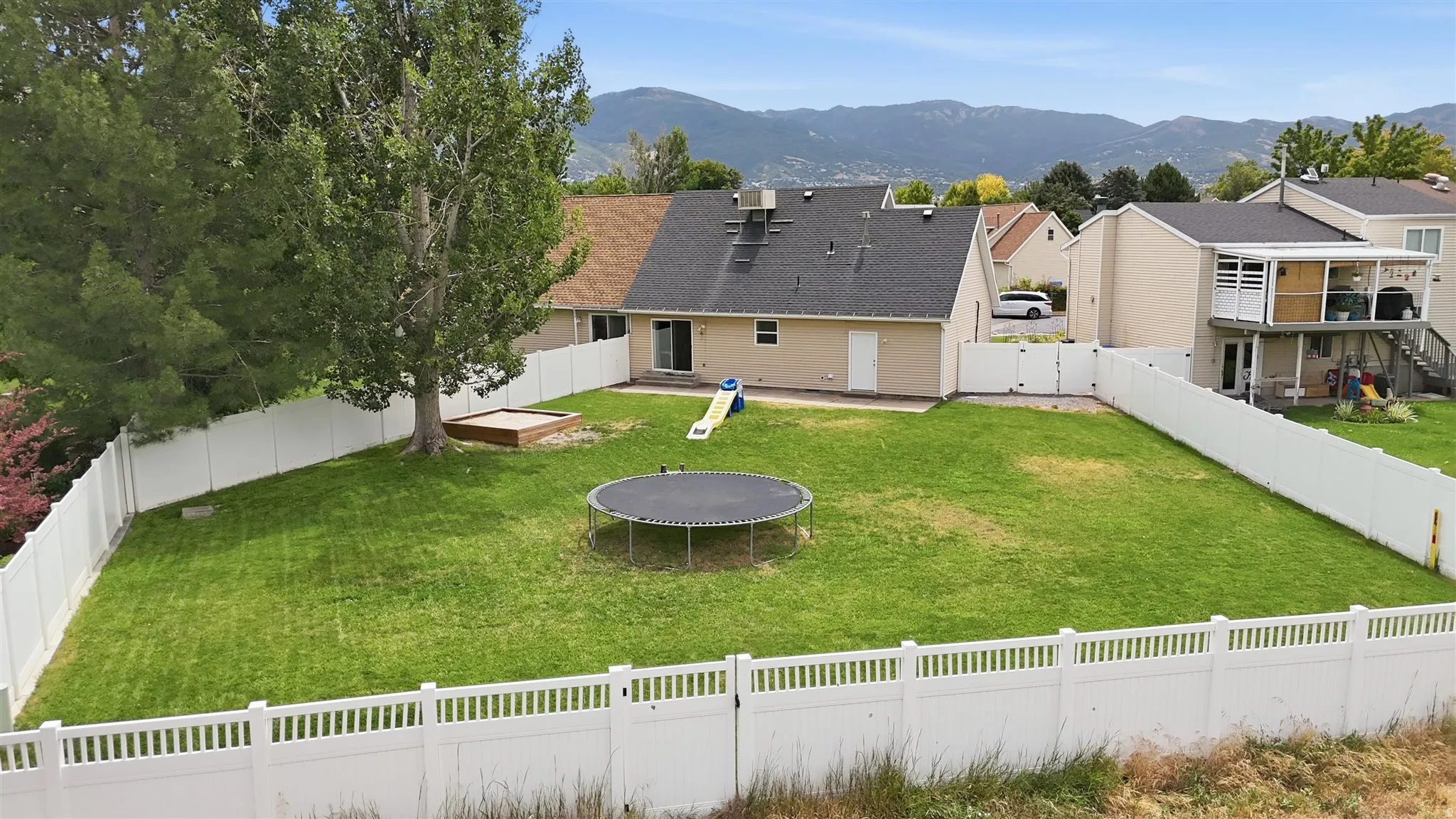 Expansive backyard featuring a manicured lawn, established trees, and a full perimeter fence