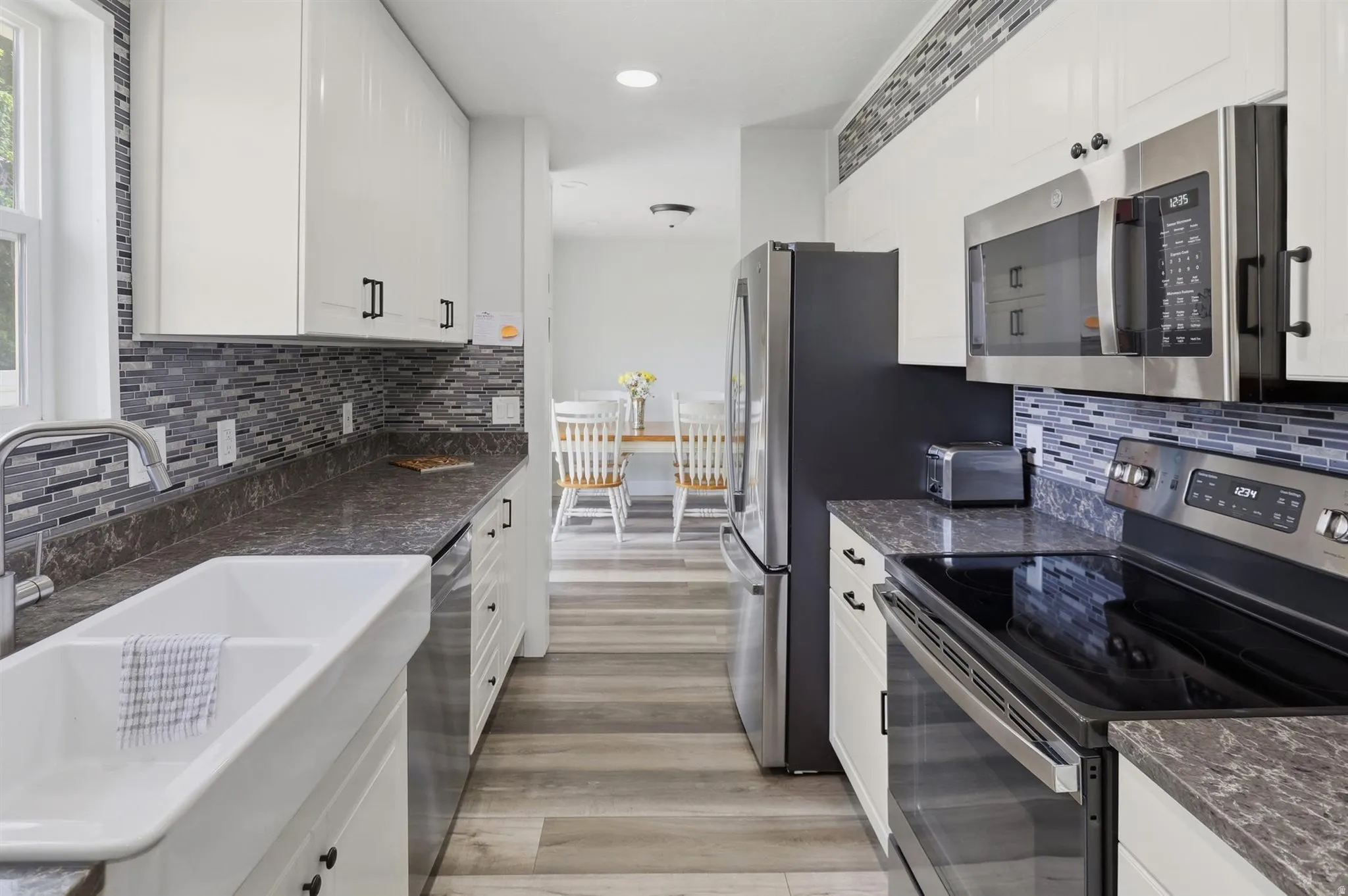 Modern kitchen featuring white cabinetry, stainless steel appliances, a mosaic tile backsplash, a farmhouse sink, and wood-finish flooring