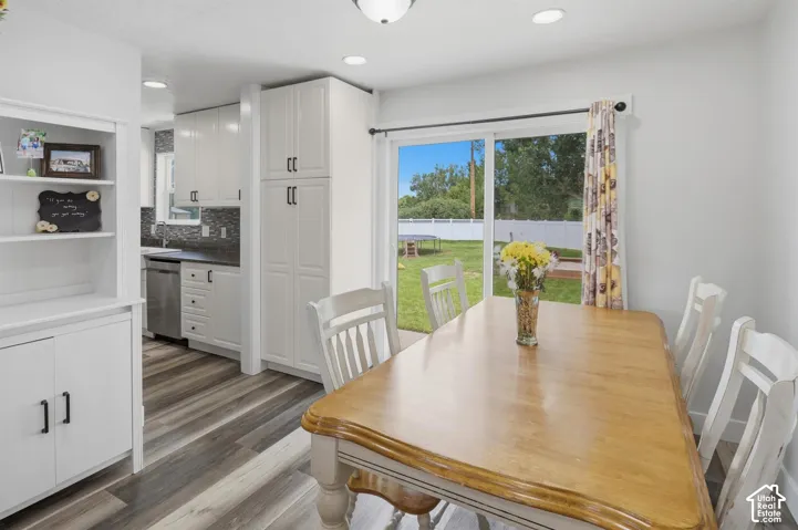 Open-concept dining area featuring wood-finish flooring, a sliding glass door to the backyard, recessed lighting, white built-in cabinetry, and a kitchen with stainless steel appliances and a dark tile backsplash