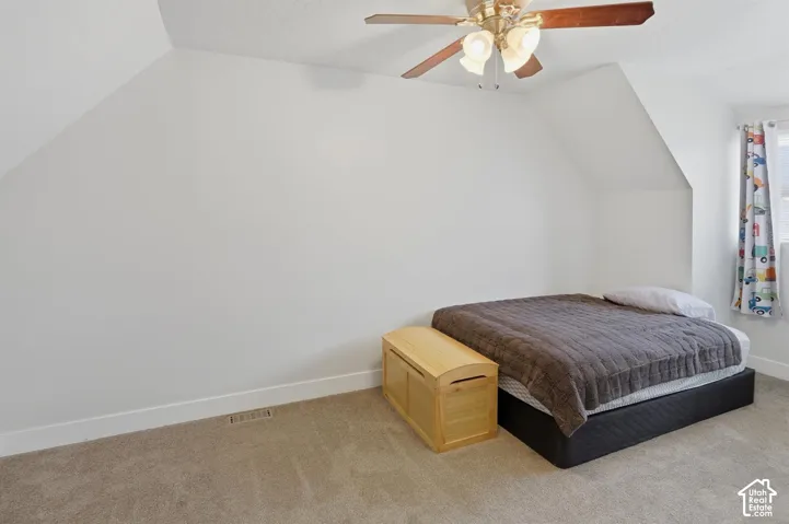 Room featuring an angled ceiling, soft carpet flooring, and a ceiling fan with integrated lighting