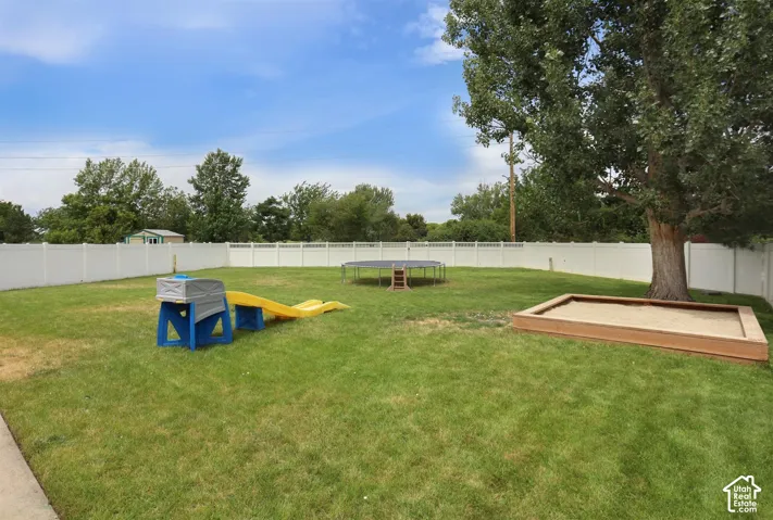 Expansive backyard featuring a manicured lawn, complete white vinyl fencing, a large mature tree, and a built-in sandbox