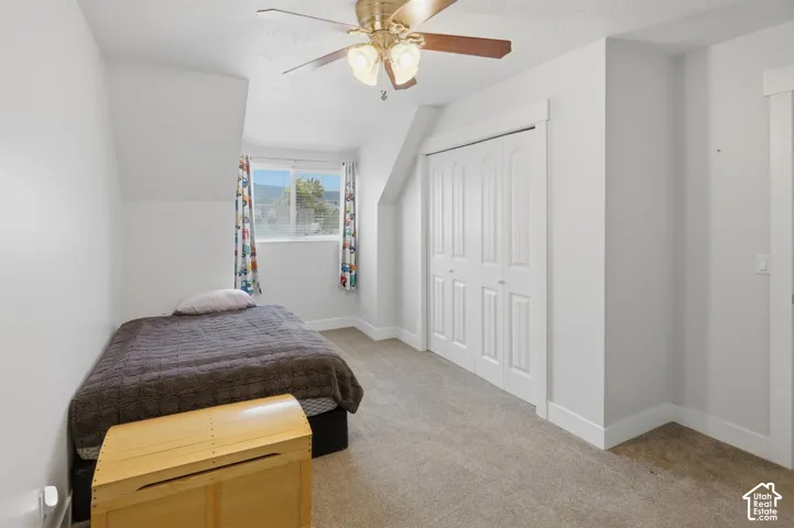 Carpeted room featuring a ceiling fan with light fixture, white walls, and a window with a mountain backdrop
