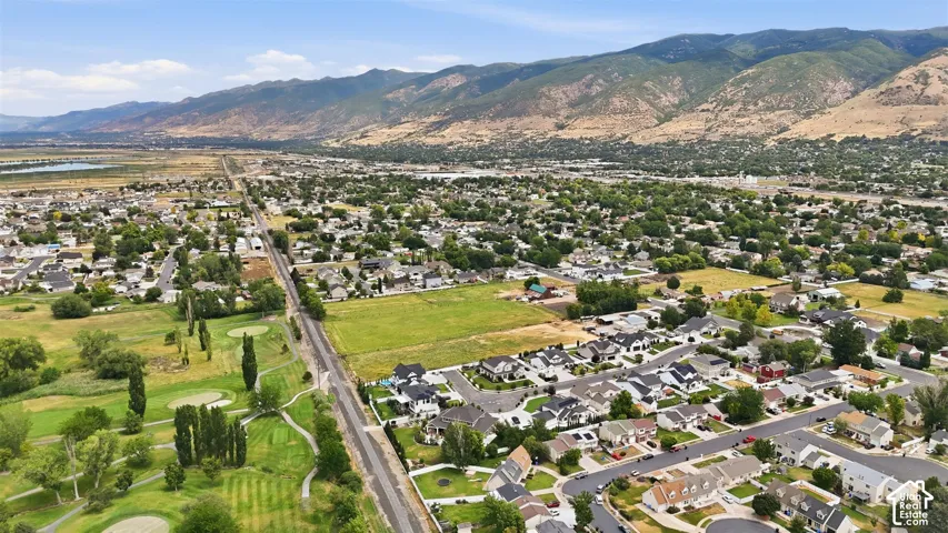 Expansive aerial view of a residential area featuring a golf course, mountain backdrop, and tree-lined streets