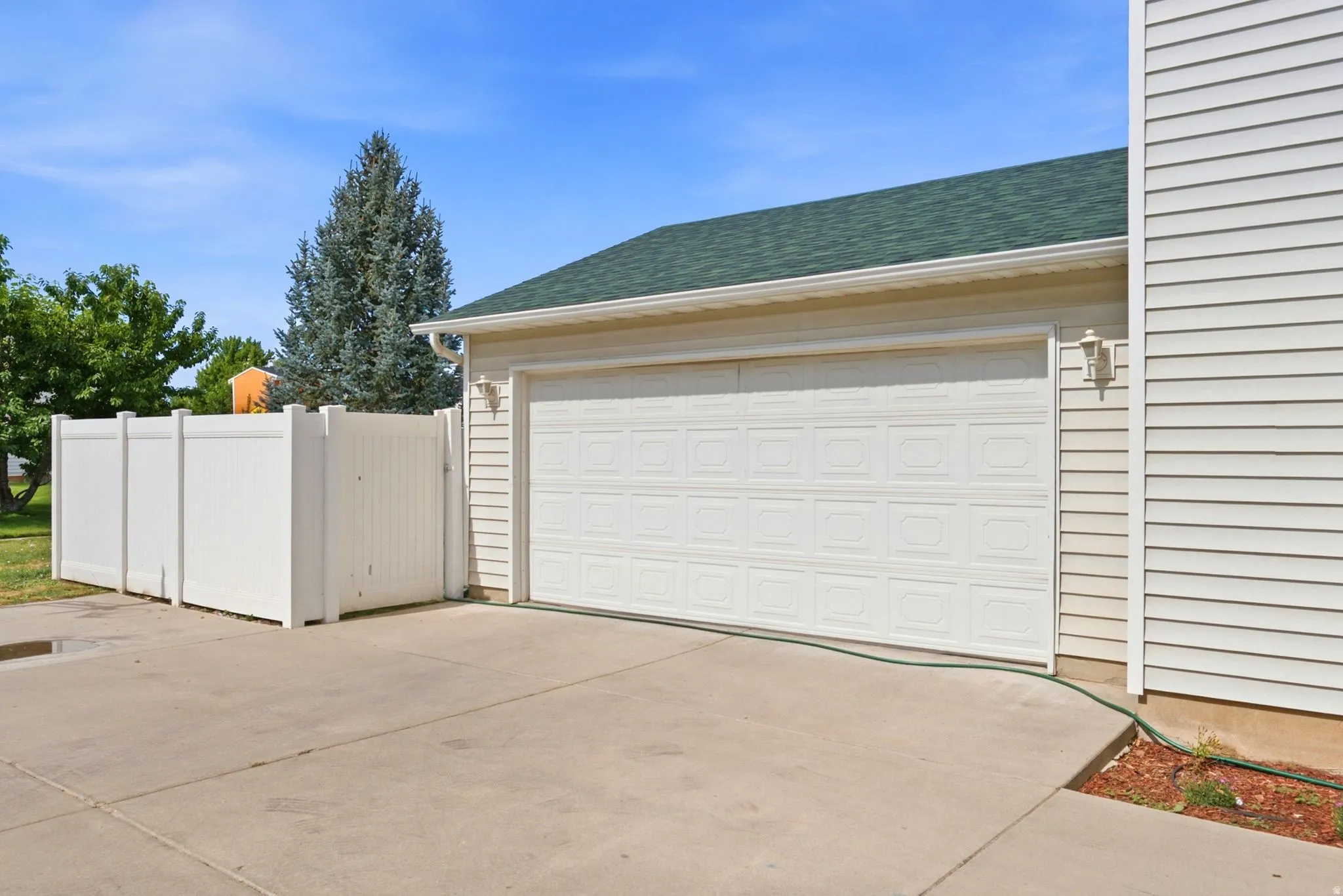 Attached two-car garage featuring a paneled door, light-colored siding, and a contrasting green-shingled roof