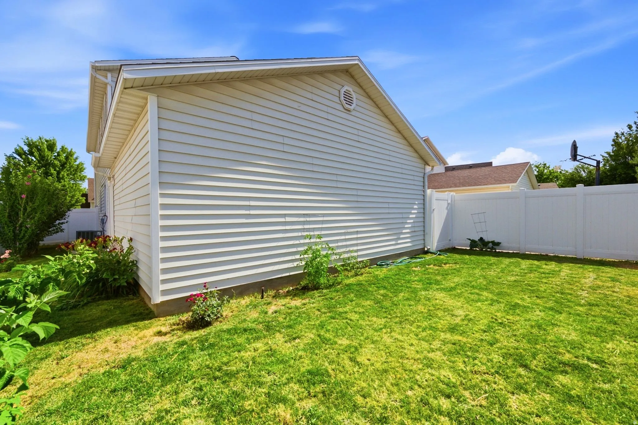 Expansive green lawn bordering the property, white vinyl fencing, and light-colored siding