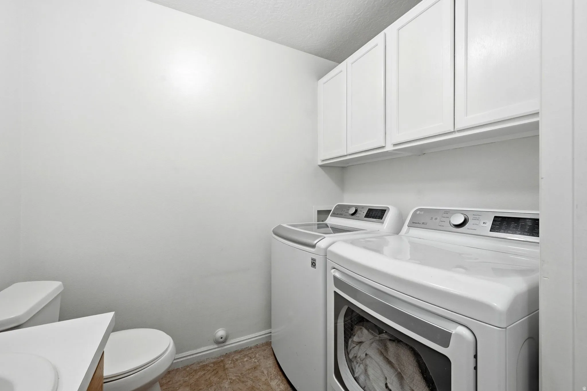 Laundry area featuring white cabinetry, a front-load washing machine, and a top-load washing machine