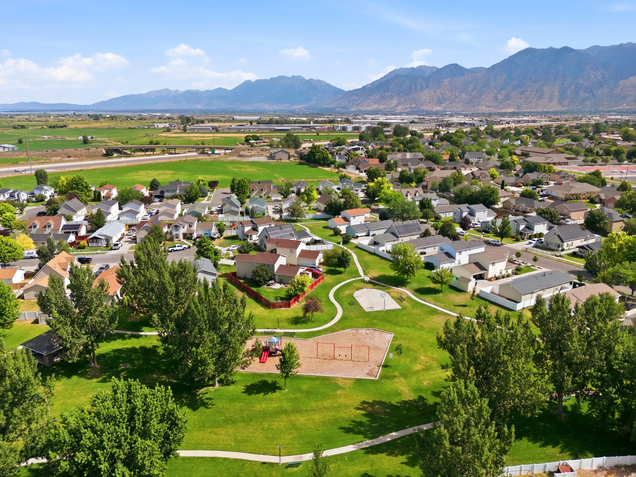Expansive community green space with mature trees, paved walking paths, and a playground