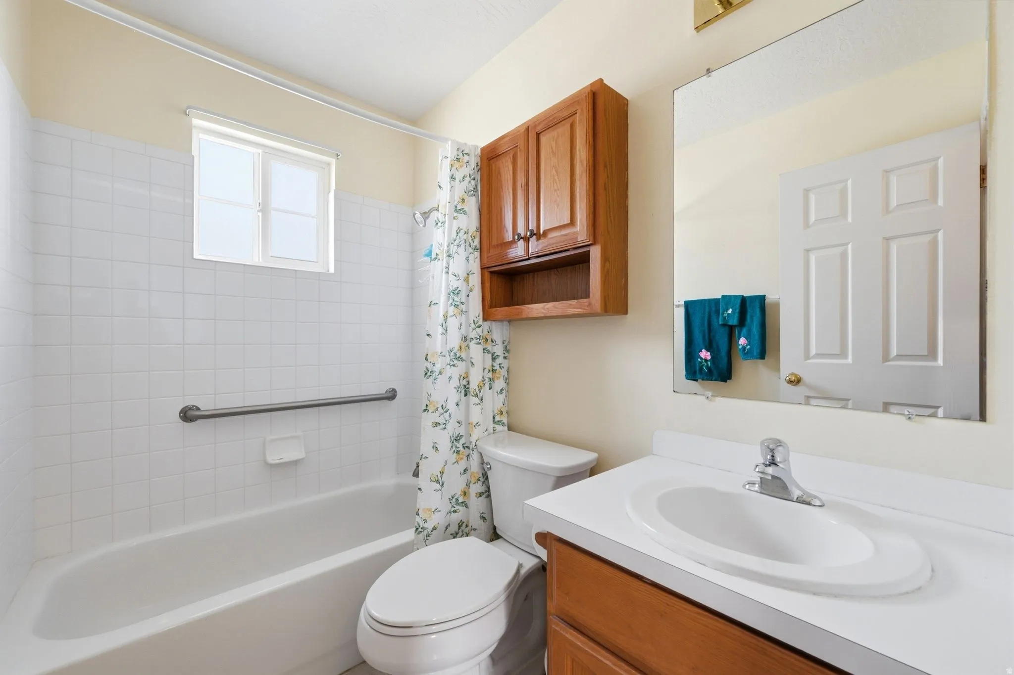 Bathroom featuring a built-in bathtub with white tile surround, a single vanity with an integrated sink, a wall-mounted mirror, and a wood-finish medicine cabinet