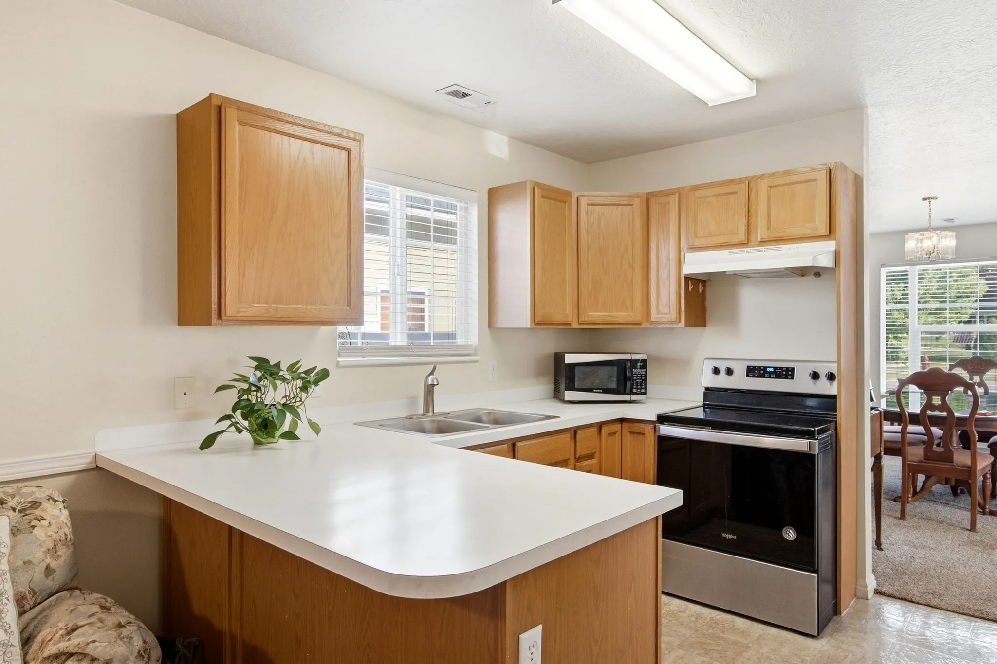 Kitchen featuring light wood-finish cabinetry, white countertops, and a double-basin stainless steel sink with a gooseneck faucet