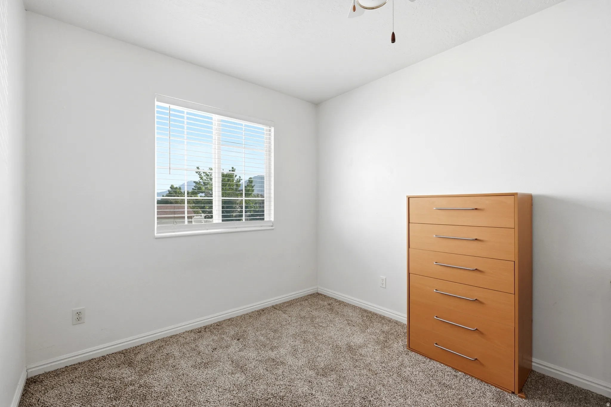 Bedroom featuring a window with horizontal blinds, neutral carpet flooring, white baseboards, and a ceiling fan with integrated lighting