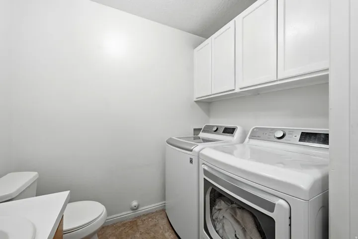 Laundry area featuring white cabinetry, a front-load washing machine, and a top-load washing machine