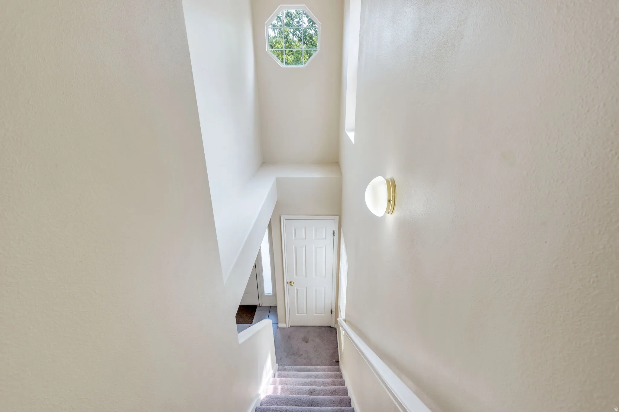 Stairwell featuring an octagonal window, high ceilings, and a wall-mounted sconce