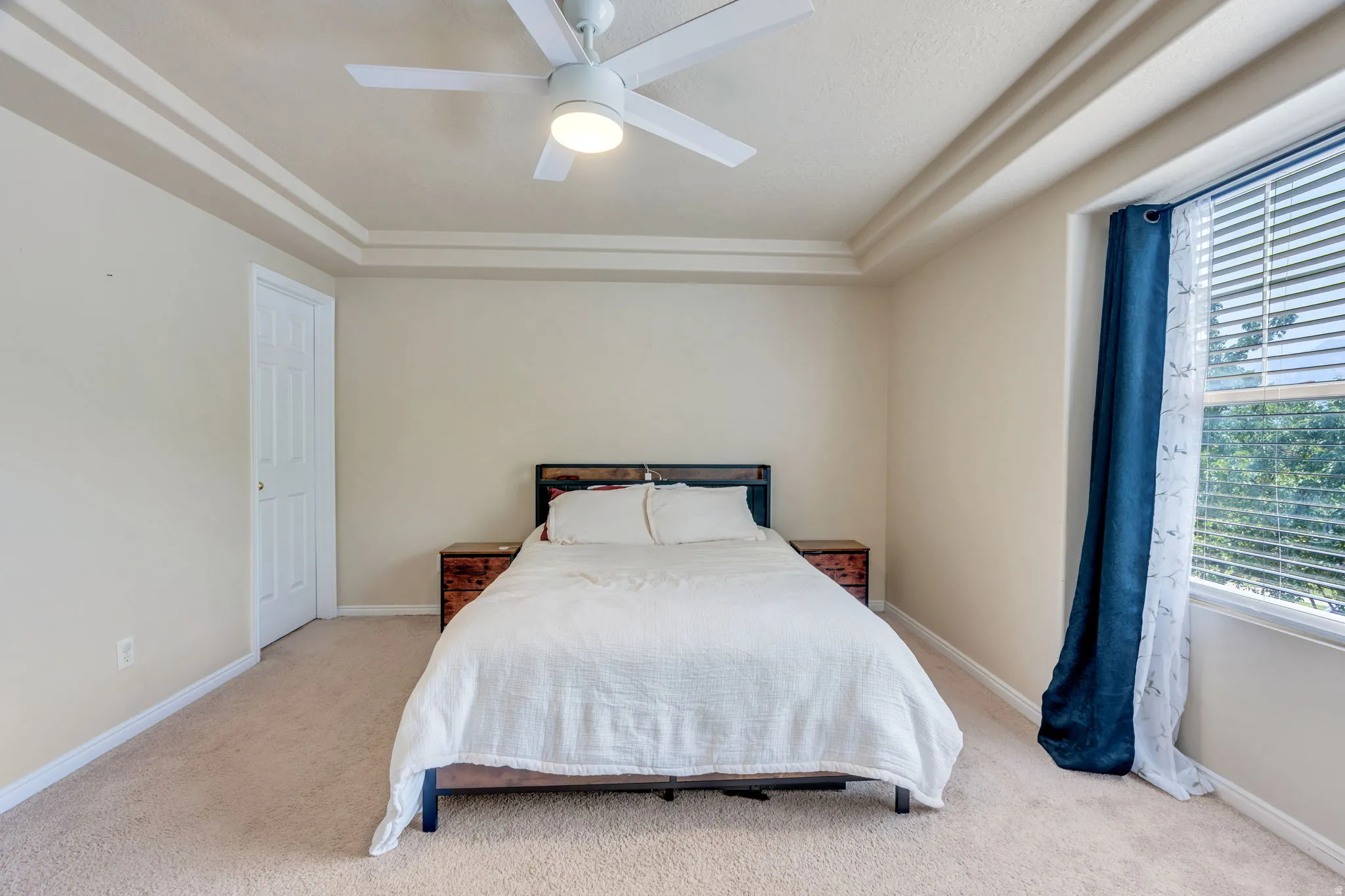 Carpeted sleeping area with a tray ceiling and ceiling fan