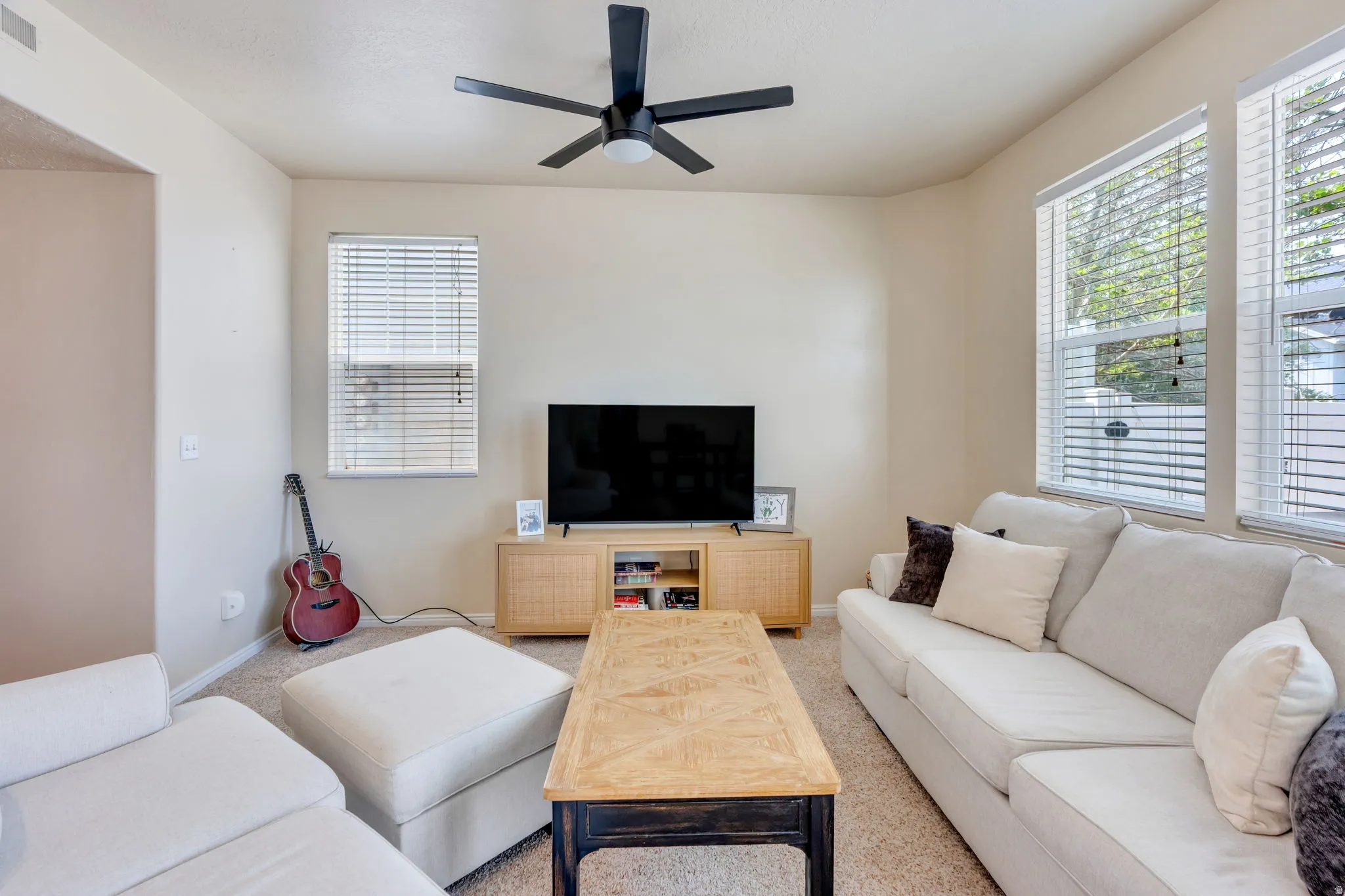 Bright interior space featuring a matte black ceiling fan, multiple windows with blinds, a built-in media console, and neutral wall paint