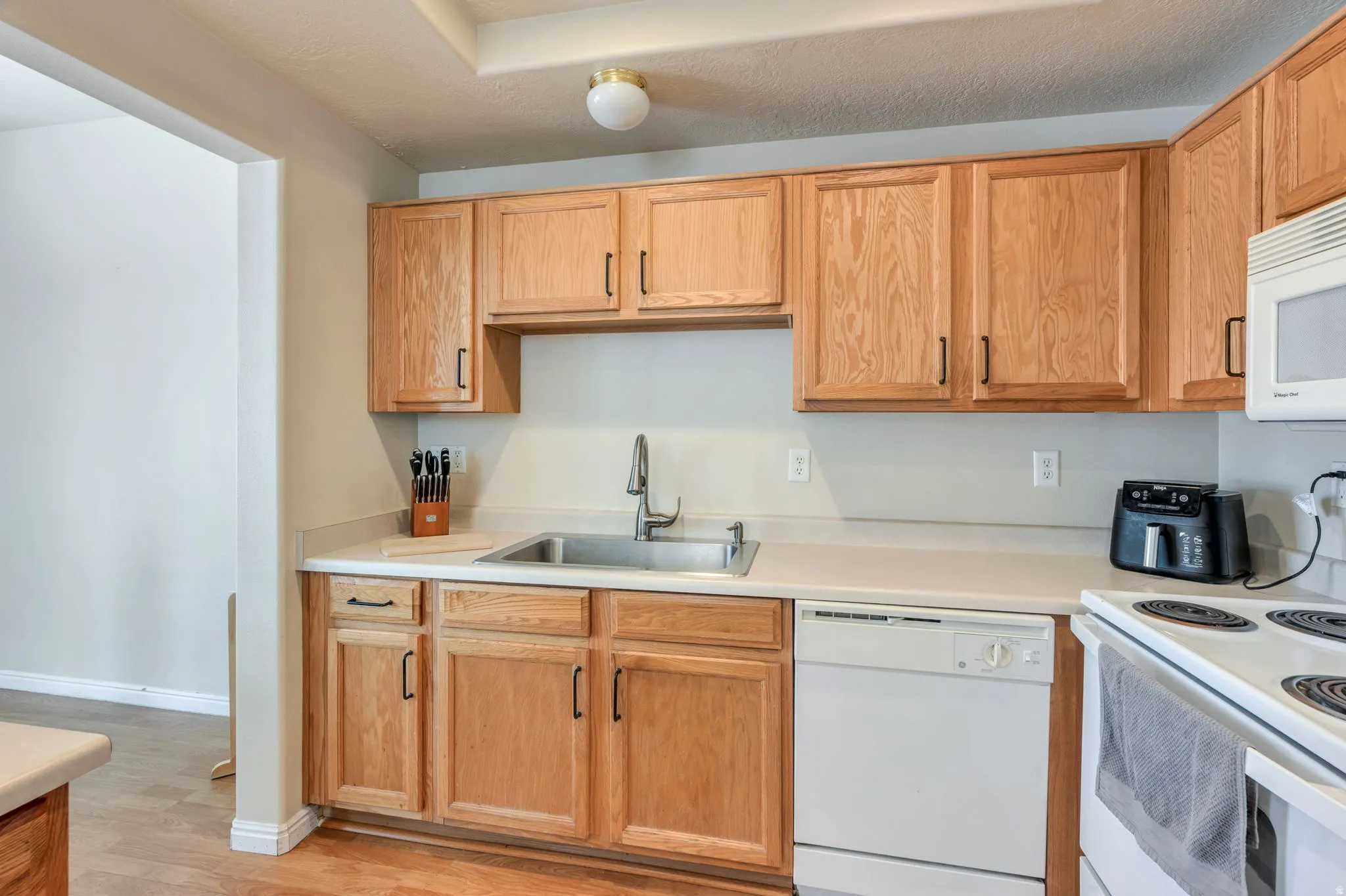 Kitchen featuring wood-finish cabinetry, white countertops, stainless steel sink, and a white dishwasher