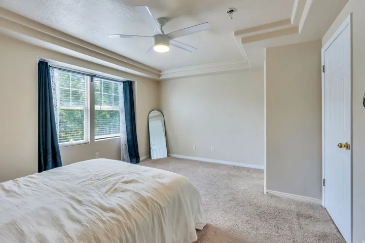 Spacious room featuring a tray ceiling with crown molding, a ceiling fan with integrated lighting, and two large windows with blinds