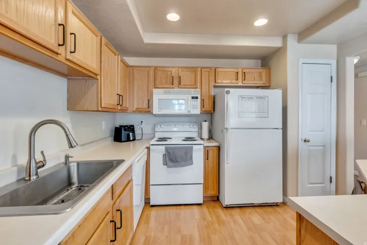 Full kitchen featuring wood-finish cabinetry, white countertops, a stainless steel double basin sink, and wood-finish flooring