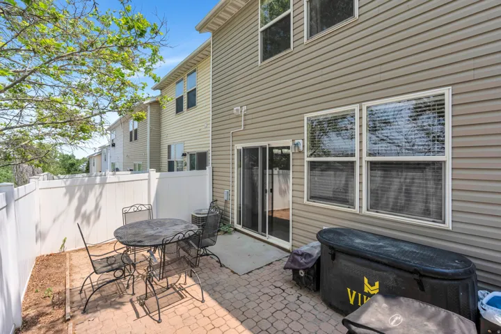 Private paved patio area featuring a white vinyl privacy fence and direct access to interior spaces via sliding glass doors