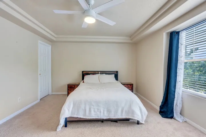 Carpeted sleeping area with a tray ceiling and ceiling fan