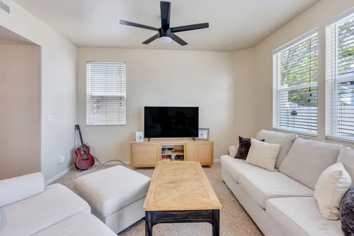 Bright interior space featuring a matte black ceiling fan, multiple windows with blinds, a built-in media console, and neutral wall paint