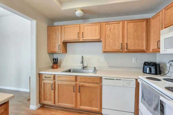 Kitchen featuring wood-finish cabinetry, white countertops, stainless steel sink, and a white dishwasher