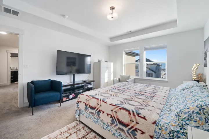 Spacious bedroom featuring light neutral carpet, a tray ceiling, two large windows, and a doorway opening to an additional interior space