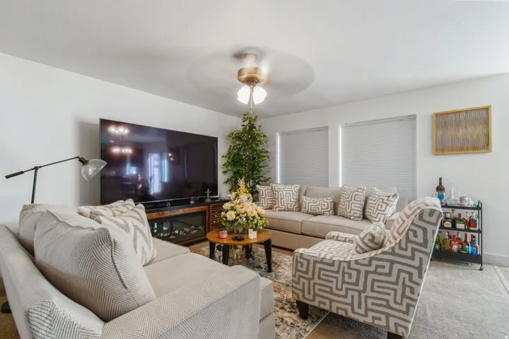 Living area featuring a ceiling fan with integrated lighting, multiple windows with blinds, and white walls
