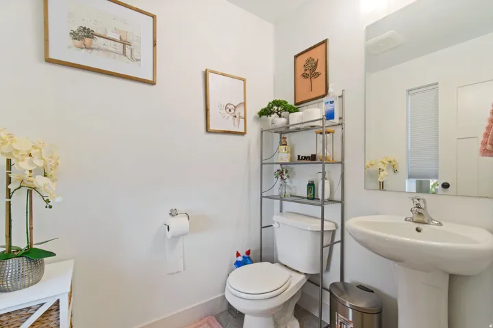 Pedestal sink with chrome faucet, wall-mounted mirror, and white toilet
