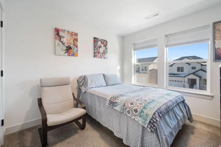 Bedroom featuring neutral wall paint, two large windows with horizontal blinds, and dark carpet flooring