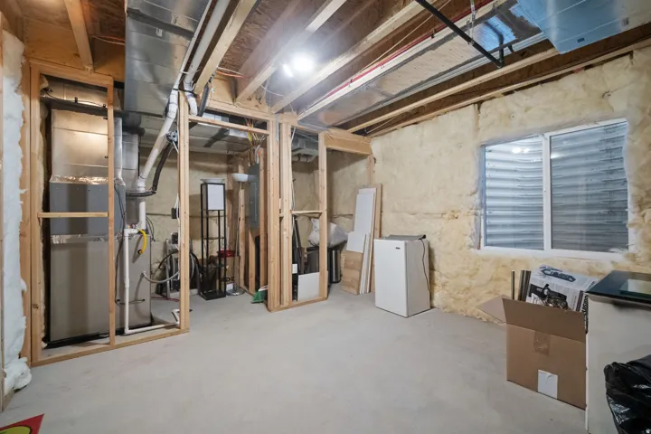 Unfinished lower level featuring exposed framing, concrete flooring, insulated exterior walls, utility sink, and a window with a window well