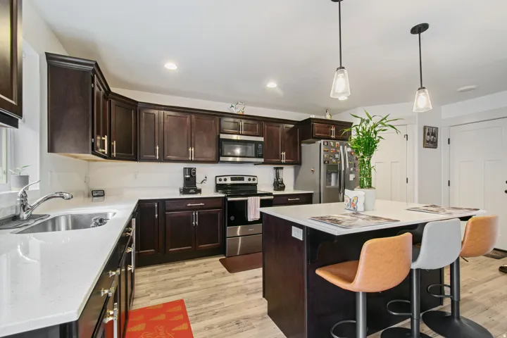 Kitchen featuring dark wood cabinetry, light-toned countertops, stainless steel appliances, a center island with seating, and wood-finish flooring