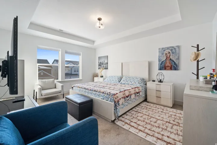 Spacious bedroom featuring a tray ceiling, dual windows, and light-colored carpeting