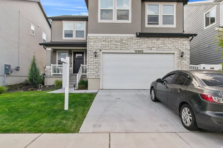 Modern exterior featuring a two-car garage, stone facade accents, a covered porch with white railings, and a concrete driveway