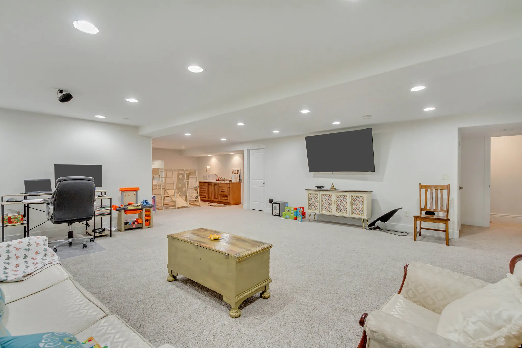 Spacious finished lower level featuring recessed lighting, light-toned carpeting, and a built-in wood vanity with a countertop and sink in the background