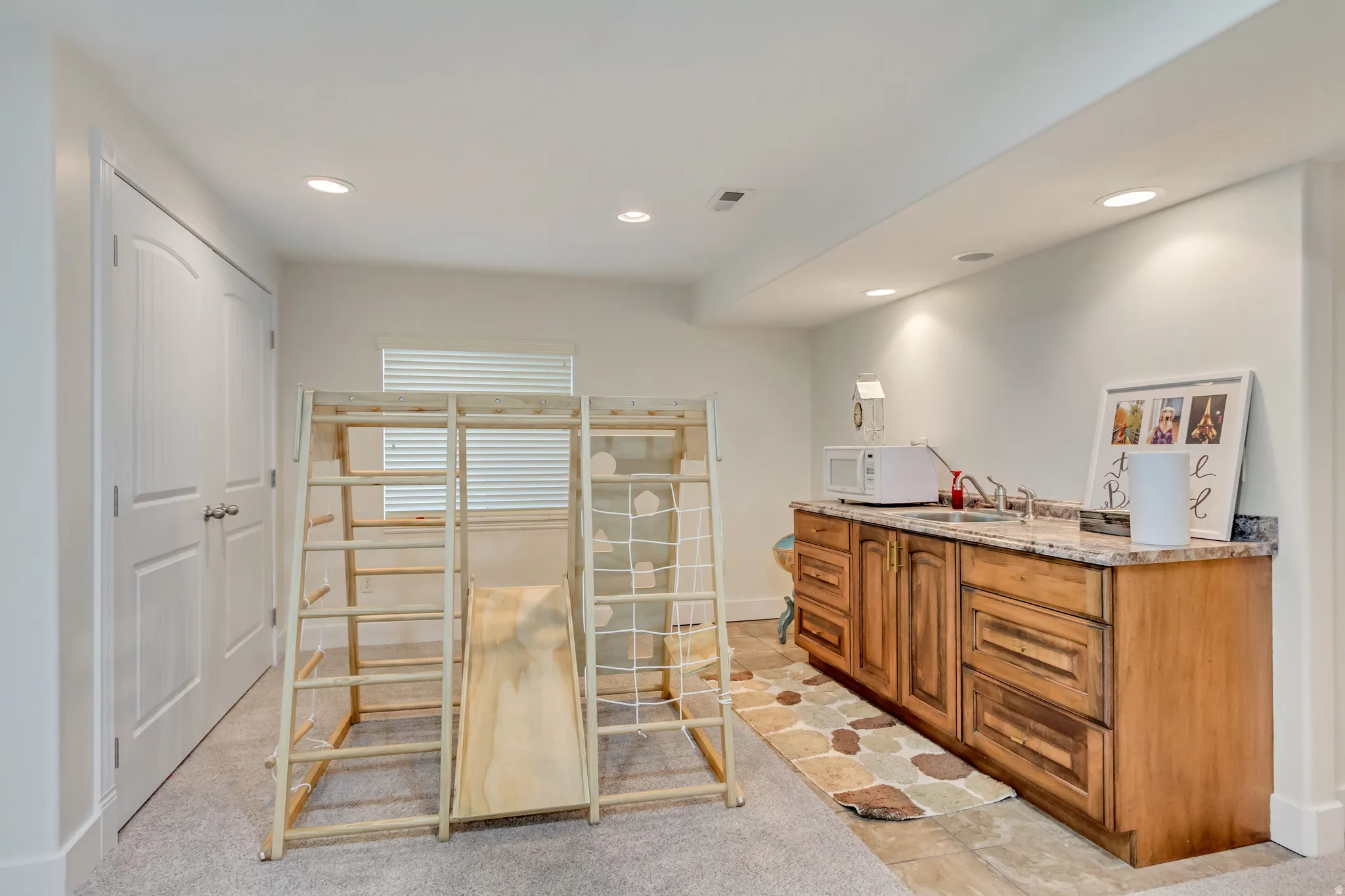 Lower-level kitchenette featuring wood cabinetry, granite-style countertops, and a stainless steel sink