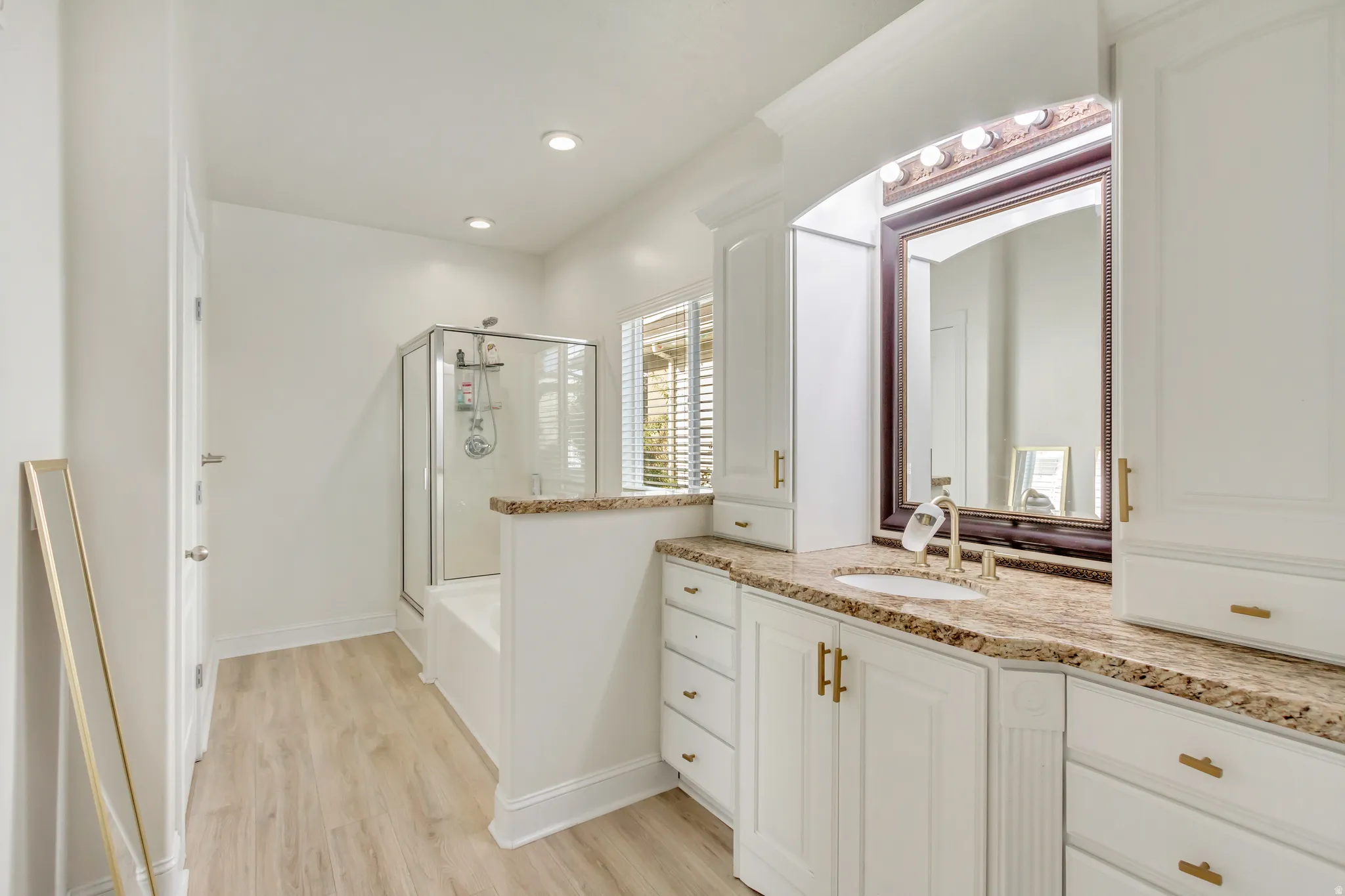 Bathroom featuring a white vanity with gold hardware, a stone countertop, and an undermount sink