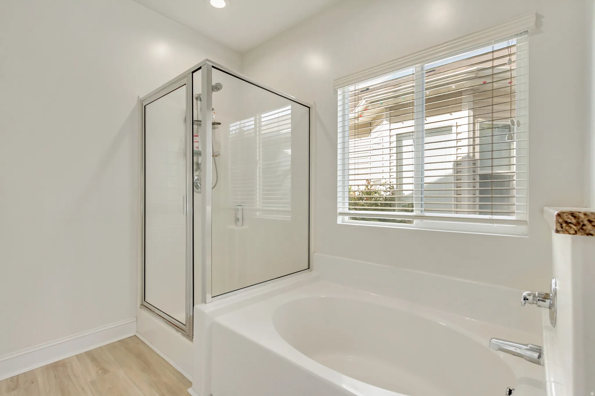 Contemporary bathroom with a built-in soaking tub, adjacent glass-enclosed shower, wood-finish flooring, and a window with horizontal blinds