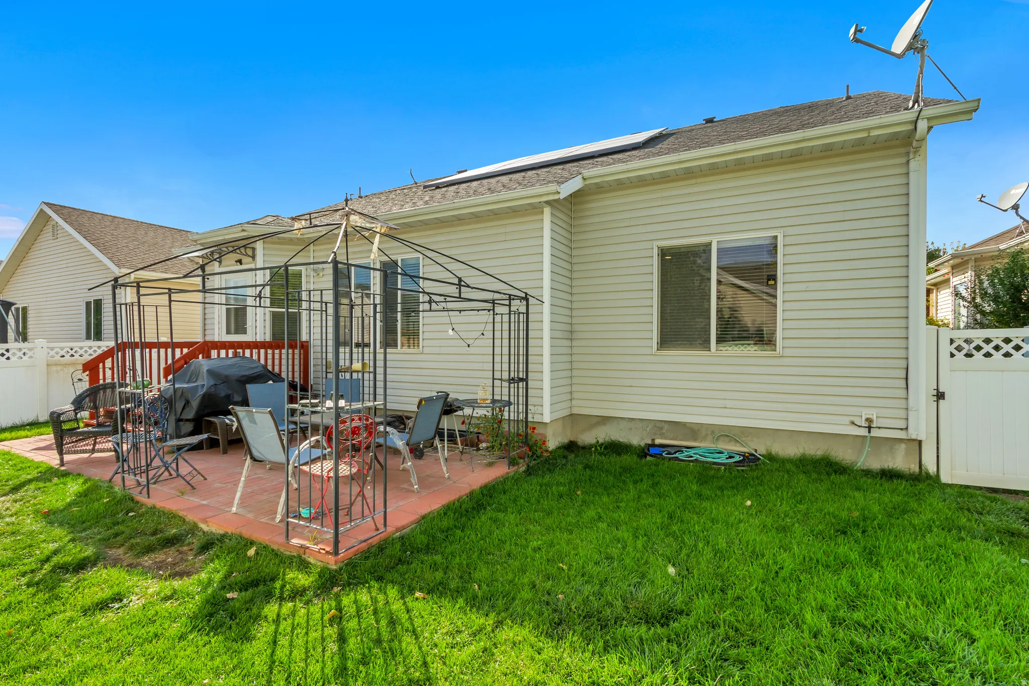 Red brick paver patio with a metal gazebo frame, a wooden deck, and a manicured lawn