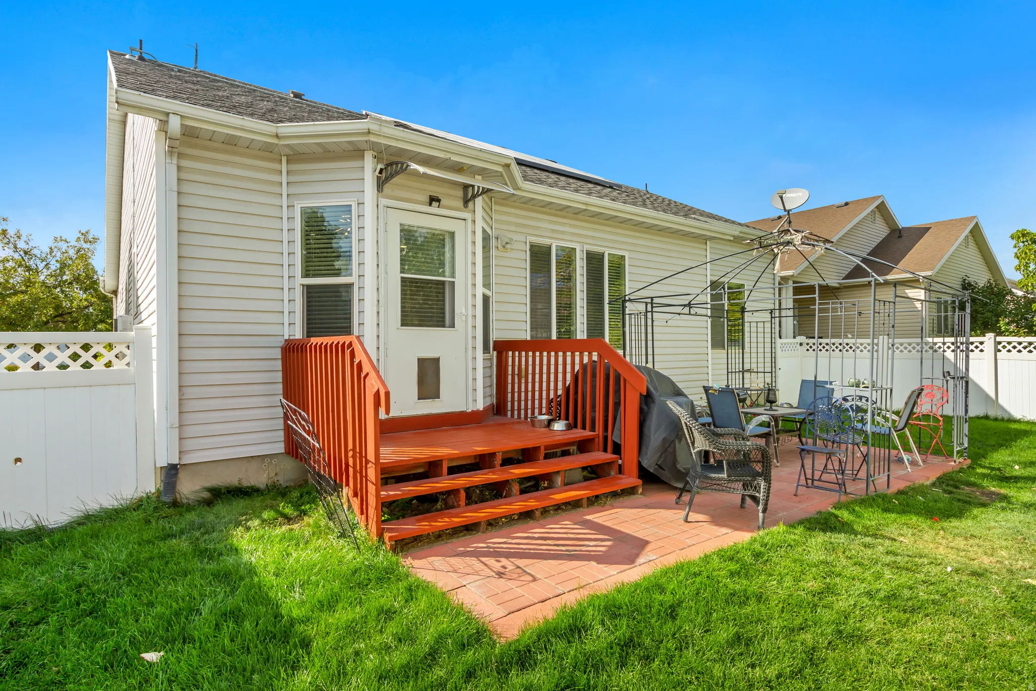 Rear exterior featuring light-colored siding, a wooden deck with red-stained steps and railings, and a brick patio