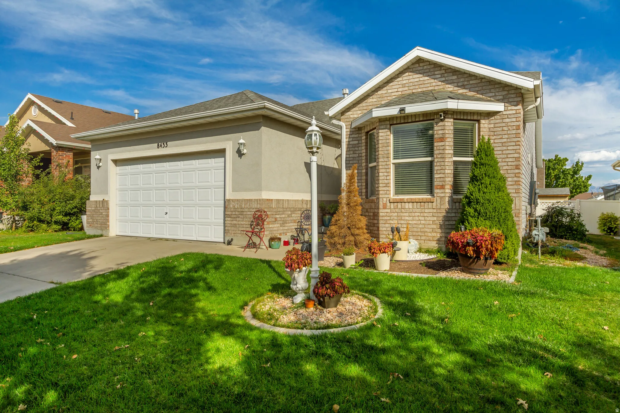 Brick and stucco exterior with an attached garage, bay window, concrete driveway, and a landscaped front yard with decorative plantings