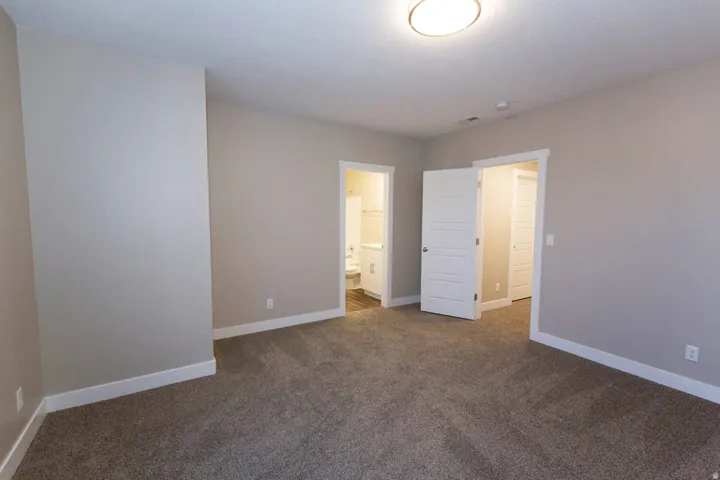 Spacious carpeted room featuring light gray wall paint, white trim, and a contemporary ceiling light fixture