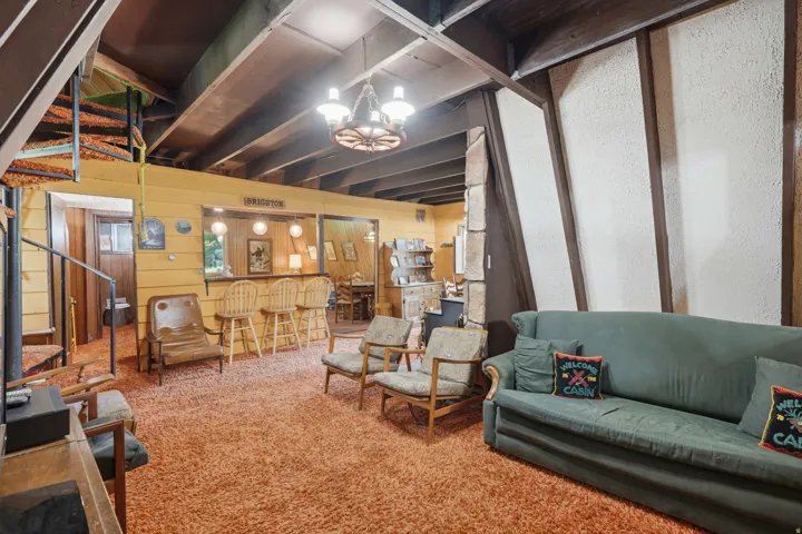Recreational space featuring a built-in bar with seating, exposed ceiling beams, a spiral staircase, textured wall panels, and a wagon wheel chandelier