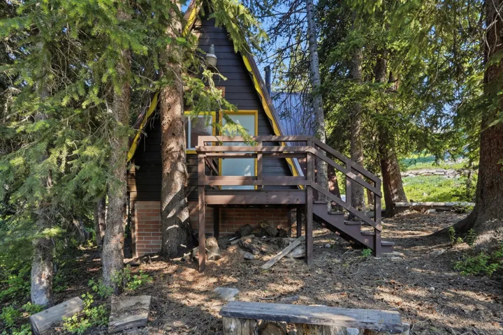 A-frame cabin featuring a dark exterior, brown deck with railings, and a brick foundation