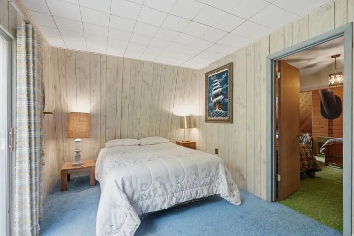 Bedroom featuring light wood-finish paneled walls, blue carpeting, and a drop ceiling