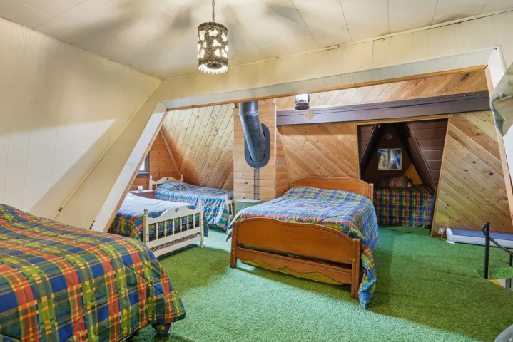 Sloped attic room featuring wood-paneled walls and ceilings, green carpet flooring, a central pendant light fixture, and built-in alcove sleeping areas